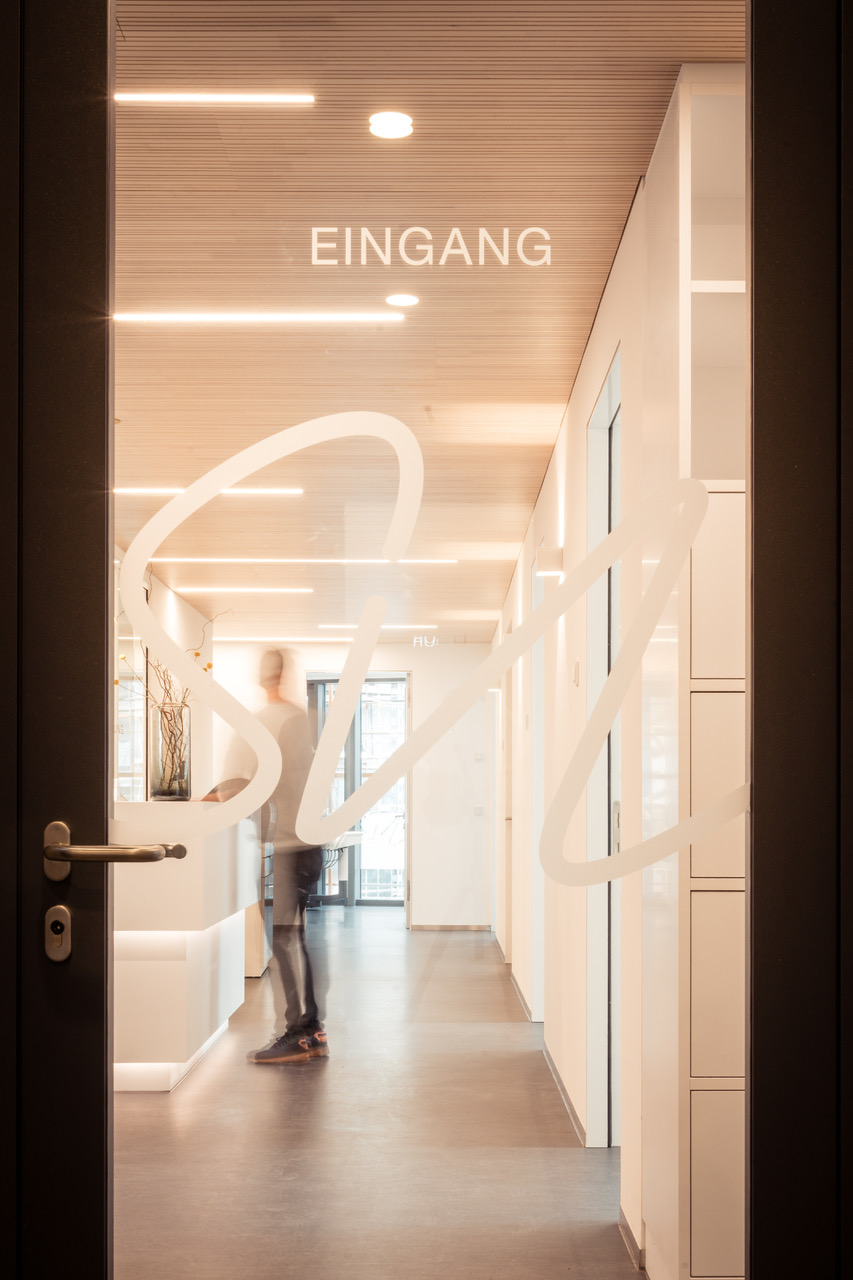 Zahnmedizin an der Lokhalle – zahnärztliche Kompetenz mit Herz 2 Glastür mit dem Schriftzug Eingang und Praxislogo, dahinter der helle Empfangsbereich.